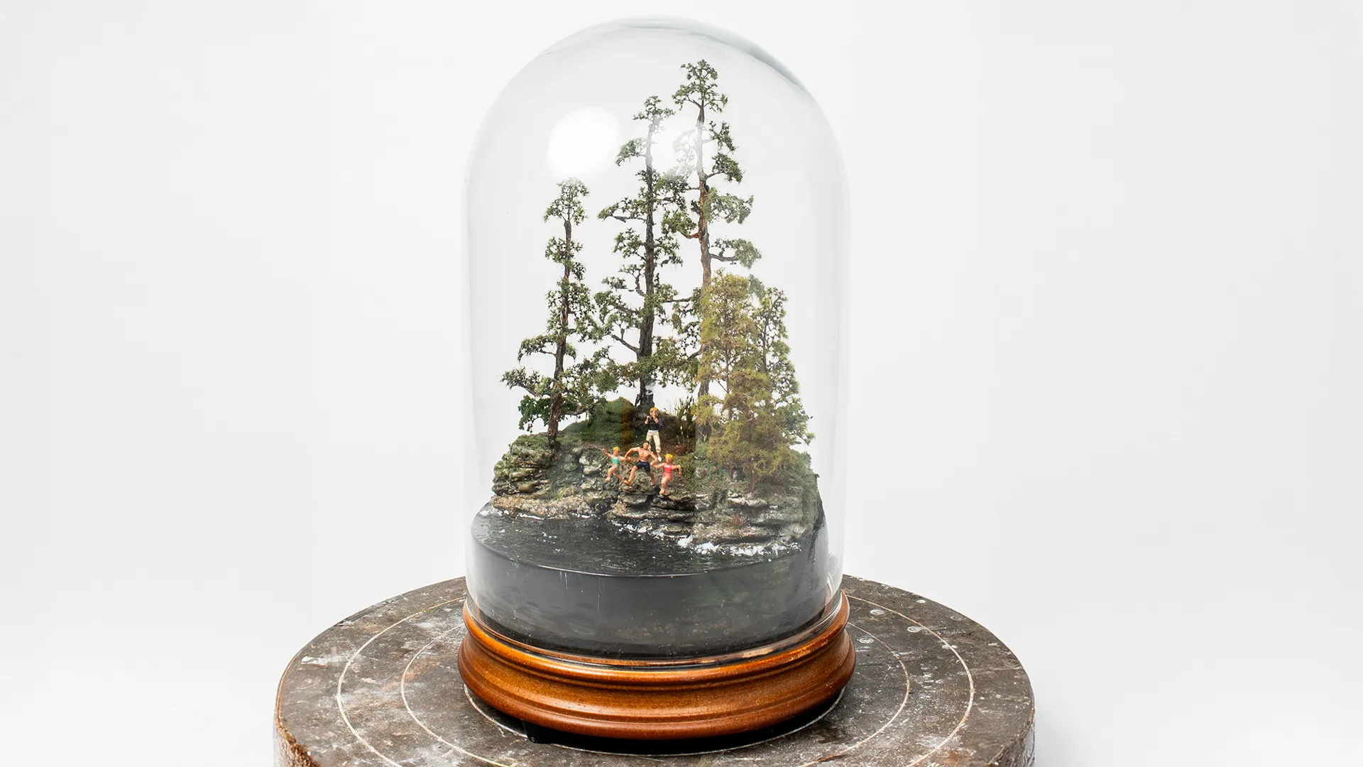 Micro landscape of a father and daughters displayed on a wooden pedestal.