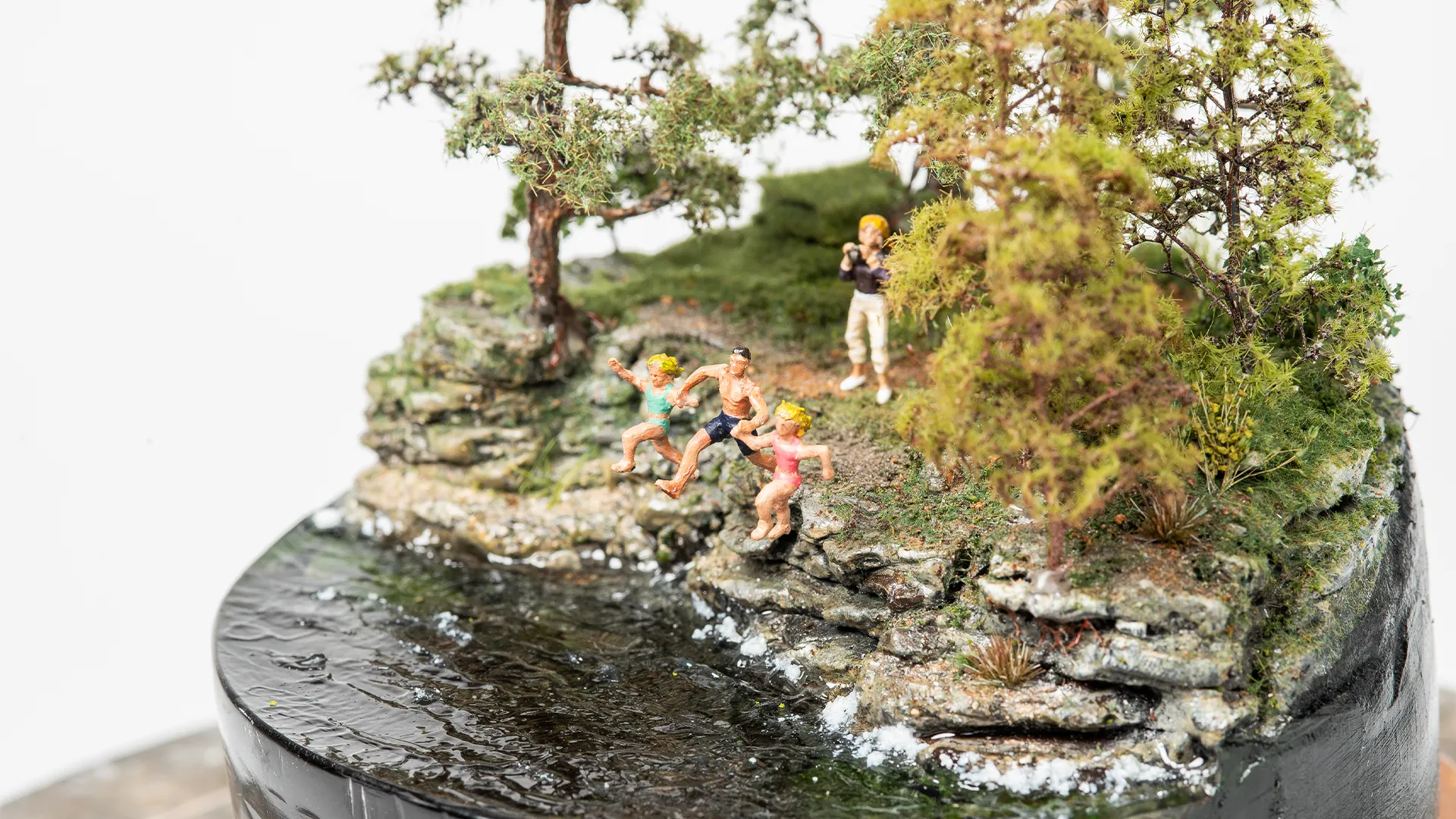 handmade-miniature-father-daughters-jump Handmade miniature artwork of a father and daughters jumping together near a lakeshore.
